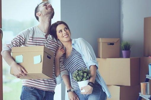 一对微笑的夫妇拿着移动的盒子和一株植物, 这是一个与联合地产(United Properties)的西密歇根物业管理公司(West Michigan property management)合作的365买球官网入口的例子